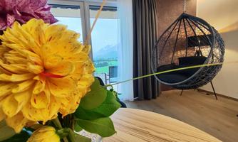 A stylish apartment with a rocking chair and large windows. In the foreground, there is a vase with colorful flowers.