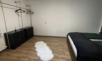 A simple bedroom with a double bed and a wooden floor. On the left side, there are wardrobes with coat hooks.