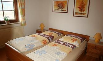 A cozy bedroom with a double bed and two nightstands. The walls are decorated with pictures of trees, and the wooden ceiling gives it a warm atmosphere.