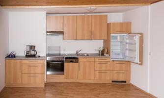 A modern kitchen with wooden cabinets and a refrigerator. The setup is functional and well-organized.