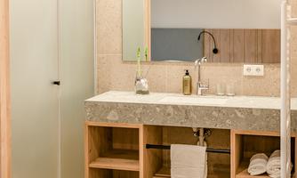 A modern bathroom with a stone sink and wooden shelves. The walls are light and the lighting is pleasant.