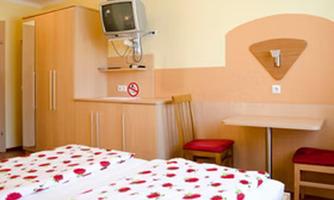 A simple room with two beds adorned with red roses. There is a table and a seating area as well as a television on the wall.