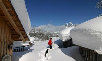 A snowy winter day with high snow drifts. A person and a dog walk along a path between the buildings.