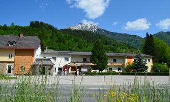 A picturesque building with colorful facades is situated in a green landscape. In the background, there are mountains with snow-capped peaks and a blue sky.