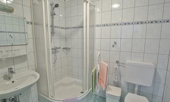 A modern bathroom with a shower cubicle and a toilet. The walls are tiled, and there is a sink as well as towels in various colors.