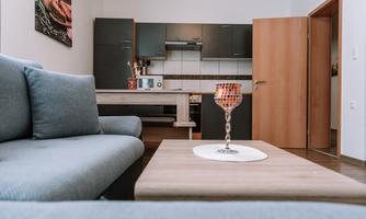 A modern apartment with an open kitchen and a cozy living room. A decorative glass sits on the table and the room is decorated in neutral colors.