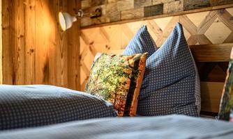 A cozy bedroom with wood paneling and a bed. On the bed lies a pillow with a nature-themed design.
