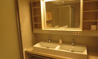A modern bathroom with two sinks and a large mirror. Shelves provide space for towels and toiletries.