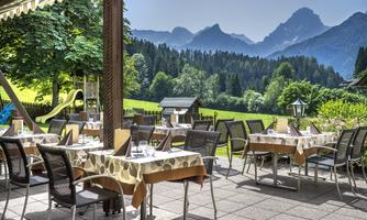 A cozy restaurant with outdoor tables and a view of the mountains. The surroundings are green and inviting.