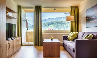 A cozy living room with a sofa and a coffee table. Large windows provide a view of the mountains and plenty of daylight.