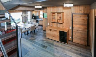 A modern kitchen with wooden furniture and a dining area. Large windows provide plenty of daylight and a cozy atmosphere.