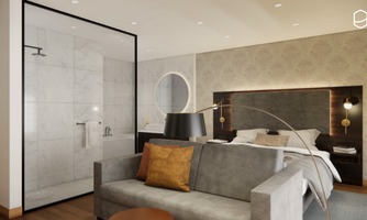 A modern hotel room with a cozy sofa and an elegant bed. The open shower is separated from the rest of the room by a glass wall.