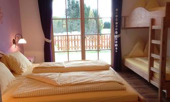 A cozy bedroom with a double bed and a bunk bed. Large windows offer views of the outdoor terrace and the garden.