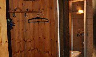 A small hallway with wooden walls and a wall-mounted cabinet. On the left side is a door to a bathroom with a shower and sink.