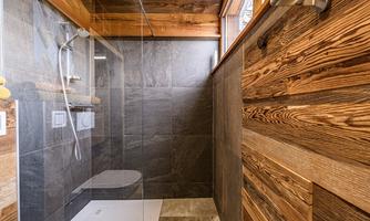 A modern shower room with elegant tiles and wood paneling. Plenty of daylight streams through the window.