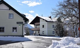 Two buildings in a snow-covered landscape, surrounded by trees. The sky is blue with a few clouds.