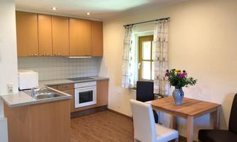 A modern kitchen with wooden cabinets and a dining area. The table is decorated with a vase full of flowers.