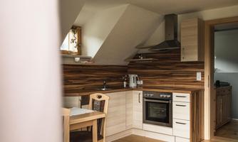 A modern kitchen with wooden details and a cooking area. The room is bright and inviting with a small table and chairs.