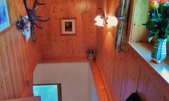 A cozy wooden staircase with rustic decor. Antlers and pictures hang on the wall, while a floral arrangement is on a table.
