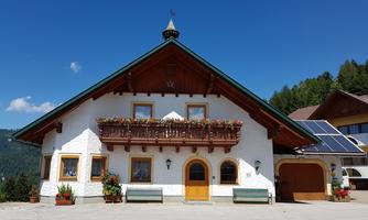 A traditional alpine house with a beautiful balcony and blooming plants. The clear blue sky and the surrounding mountains give the scene an idyllic atmosphere.