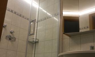 A modern bathroom with a shower and sink. The walls are tiled and well-lit.
