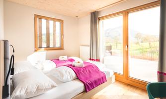 A modern bedroom with two beds and a colorful blanket. Large windows offer a magnificent view of the surrounding landscape.