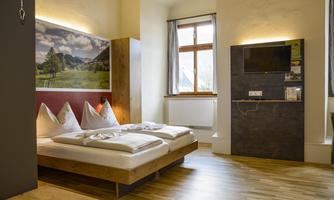 A modern bedroom with a double bed and hardwood floor. On the wall hangs a picture of a mountain landscape, and there is a window with natural light.