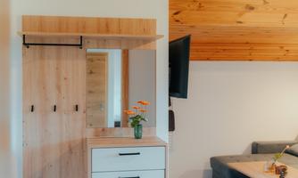 A modern hallway with a wooden wardrobe and a mirror. Next to it is a sofa and a table with a small flower vase.