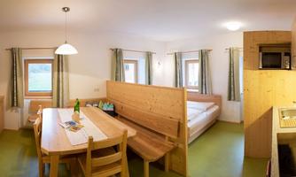 A cozy room with wooden furniture, a table and chairs. In the background, there is a bed and a small kitchenette.