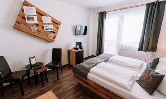 A modern hotel room with a double bed, a table and chairs. The walls are painted in light colors and there is a large window with curtains.