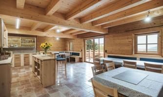 A cozy, light-filled room with a wooden ceiling and bright furniture. Sunflowers are on the table, and there is an open kitchen as well as a dining area.