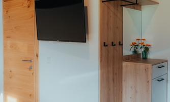 A modern entrance area with a TV on the wall and a wooden sideboard. On the sideboard, there are flowers in a vase.