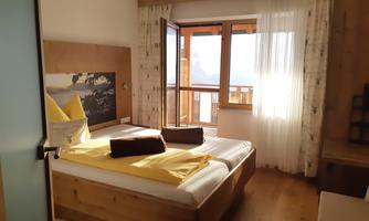 A cozy bedroom with a wooden bed and colorful pillows. The large windows offer a beautiful view outside and let in plenty of light.