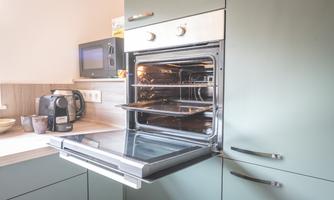 A modern kitchen with a built-in oven and a microwave in the background. The oven has a shiny surface and is well-lit.