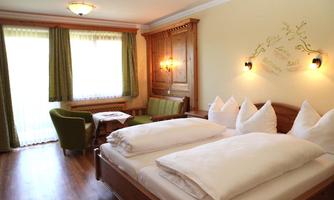 A cozy bedroom with a double bed and white pillows. The windows are decorated with green curtains and there is a seating area with a table.