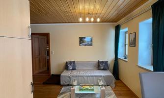 A cozy living room with wooden ceilings and large windows. There is a sofa, a coffee table, and decorative elements.