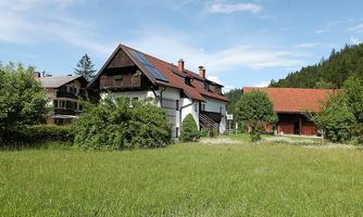 A quiet country house with green meadows and trees. The sky is blue and the surroundings are idyllic.