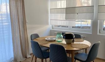 A cozy dining area with a round table and blue chairs. Large windows provide plenty of natural light.