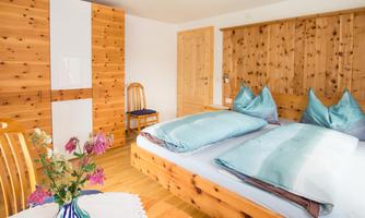 A cozy bedroom with wooden paneled walls and a large double bed. A vase with fresh flowers sits on the table.