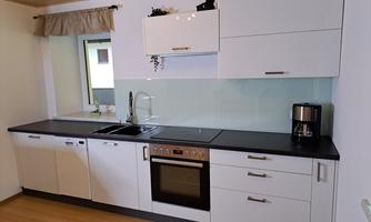 A modern kitchen with white cabinets and a dark countertop. It includes a sink, a stove, and a coffee maker.