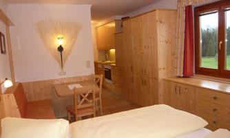 A cozy room with wooden furniture and two beds. There is a small kitchenette and a dining table with chairs.