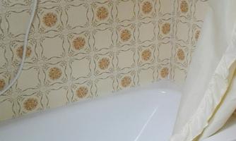 A bathroom with a bathtub and a shower head. The walls are decorated with a striking patterned tile design.