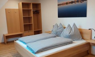 A cozy bedroom with a double bed and two pillows. The room has light wooden furniture and a picture on the wall.