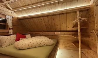 A cozy wooden room with a large bed and a red pillow. The soft lighting creates a warm atmosphere.