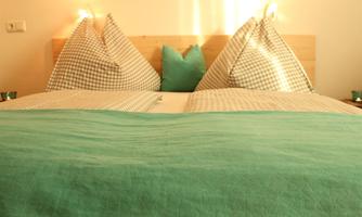 A cozy bed with checked pillows and a beautiful green blanket. The decorative lighting creates a warm atmosphere.