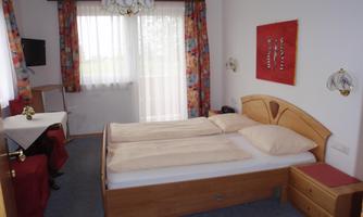 A cozy room with a double bed and colorful curtains. There is a small table and a television on the wall.