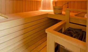 A cozy sauna with wooden paneling and warm light. The room features a wooden container and a sauna stone stove.