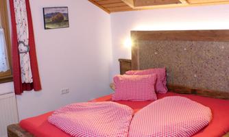 A cozy bedroom with a wooden bed and red pillows. The warm wooden structure creates an inviting atmosphere.