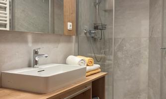 A modern bathroom with a glass shower and an elegant washbasin. There are bright towels and a cozy wood look.