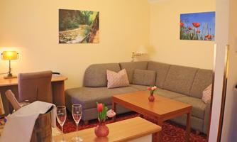 A cozy living room with a gray couch and a wooden table. Decorative pictures hang on the walls, and the room is warm and inviting.